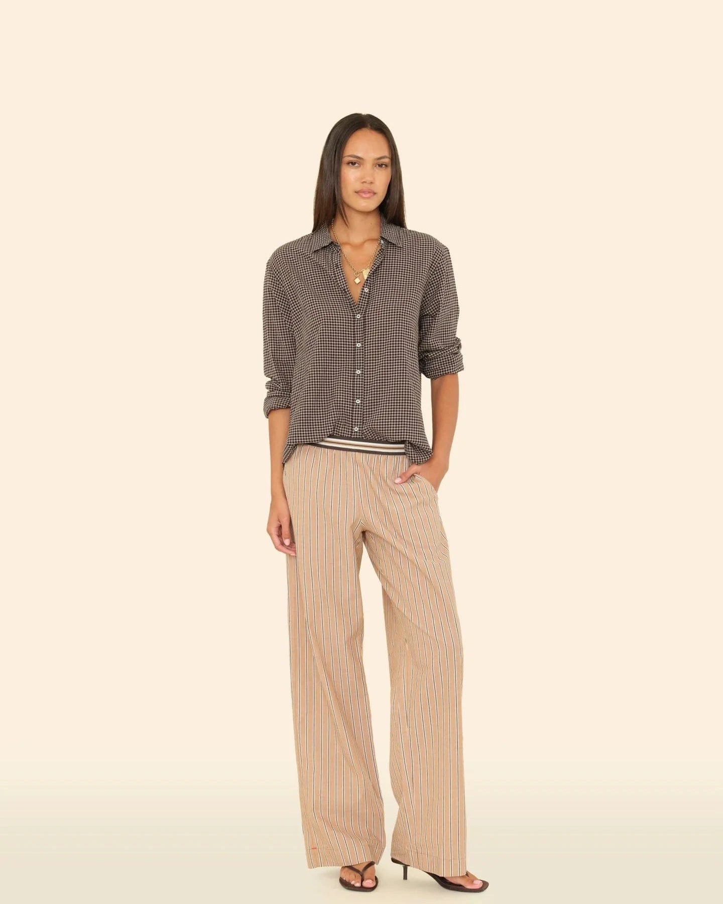 Woman wearing a gray checkered shirt and beige pants on a beige background