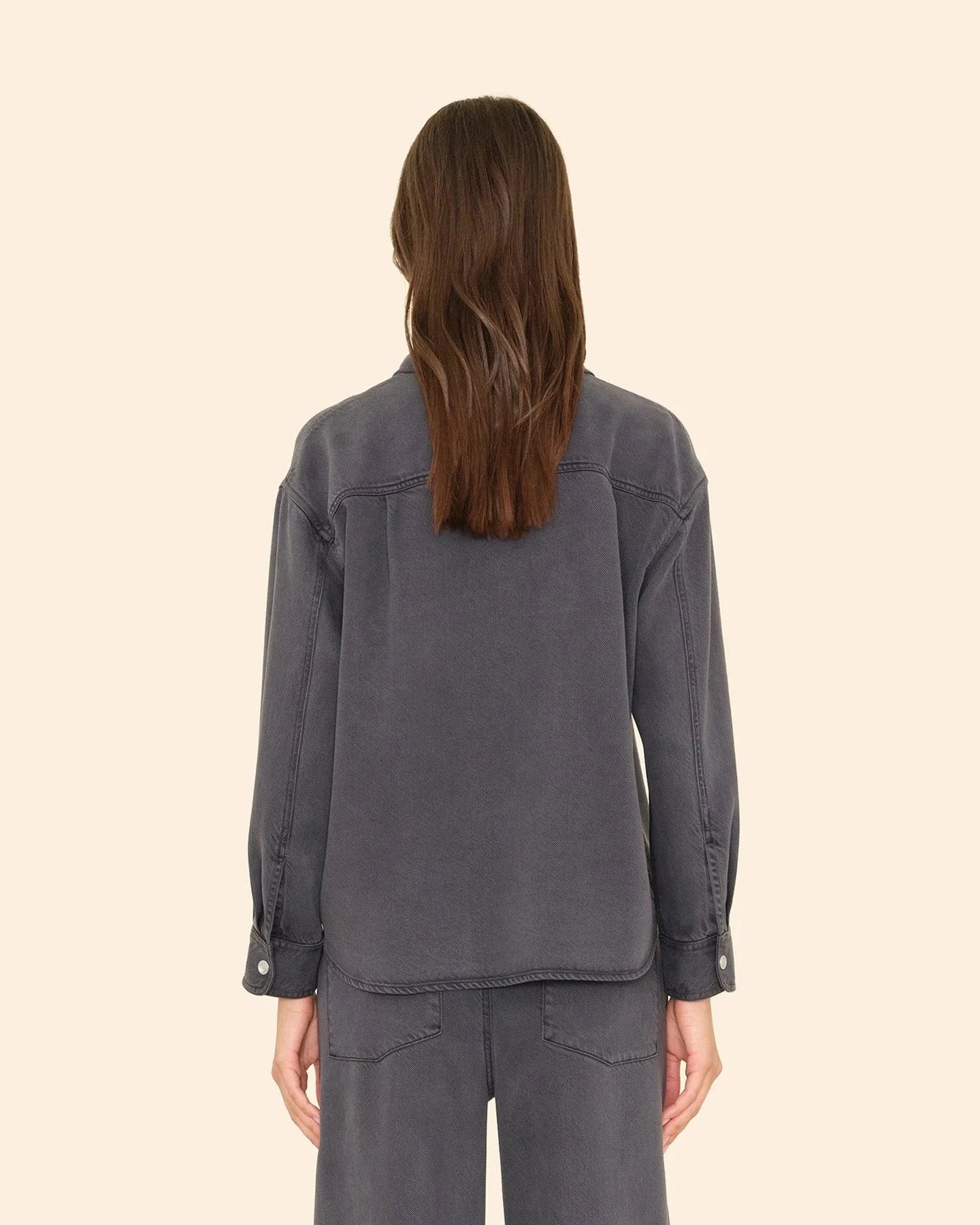 Person wearing a gray denim jacket and pants on a beige background