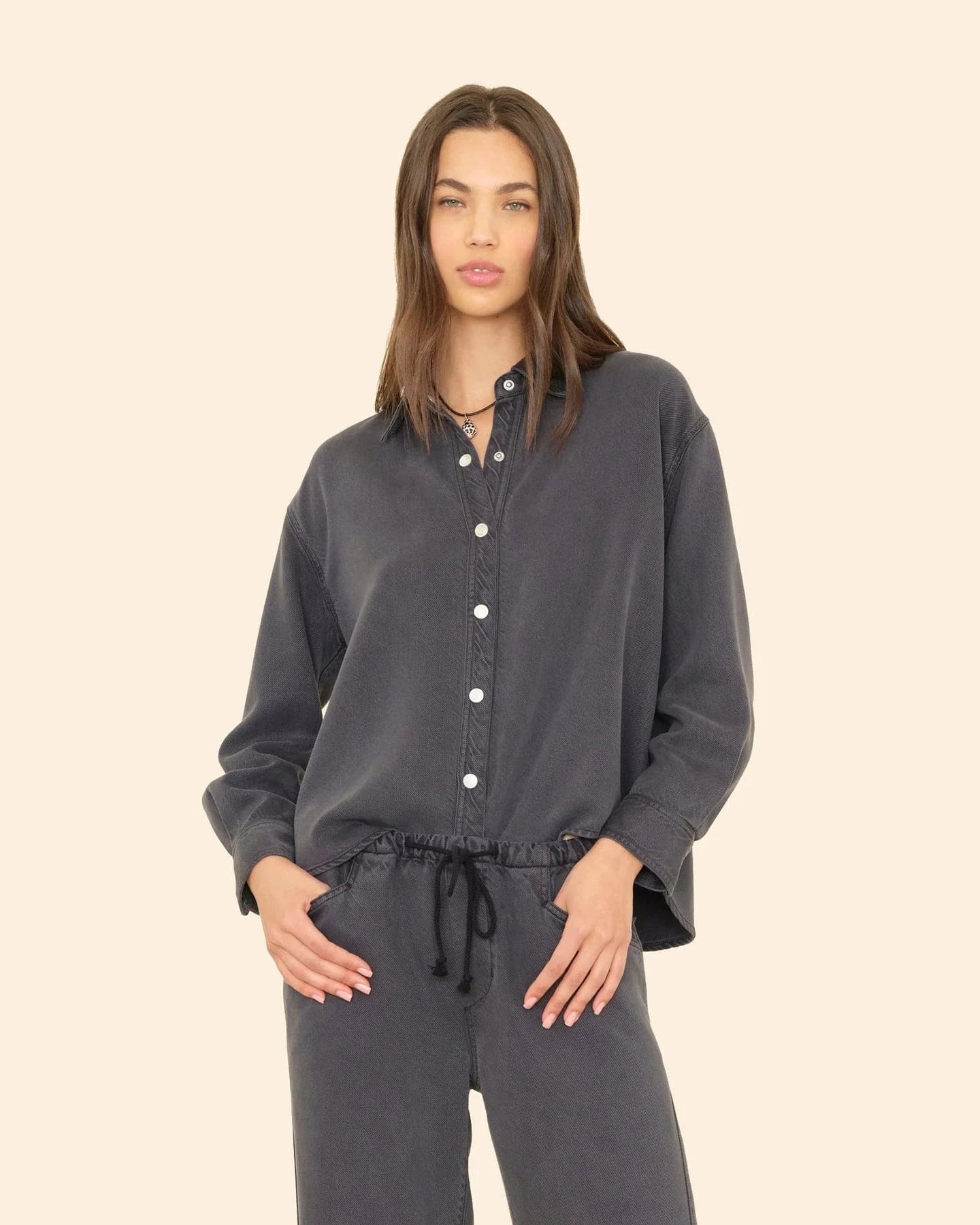 Woman wearing a dark gray button-up shirt and pants on a beige background