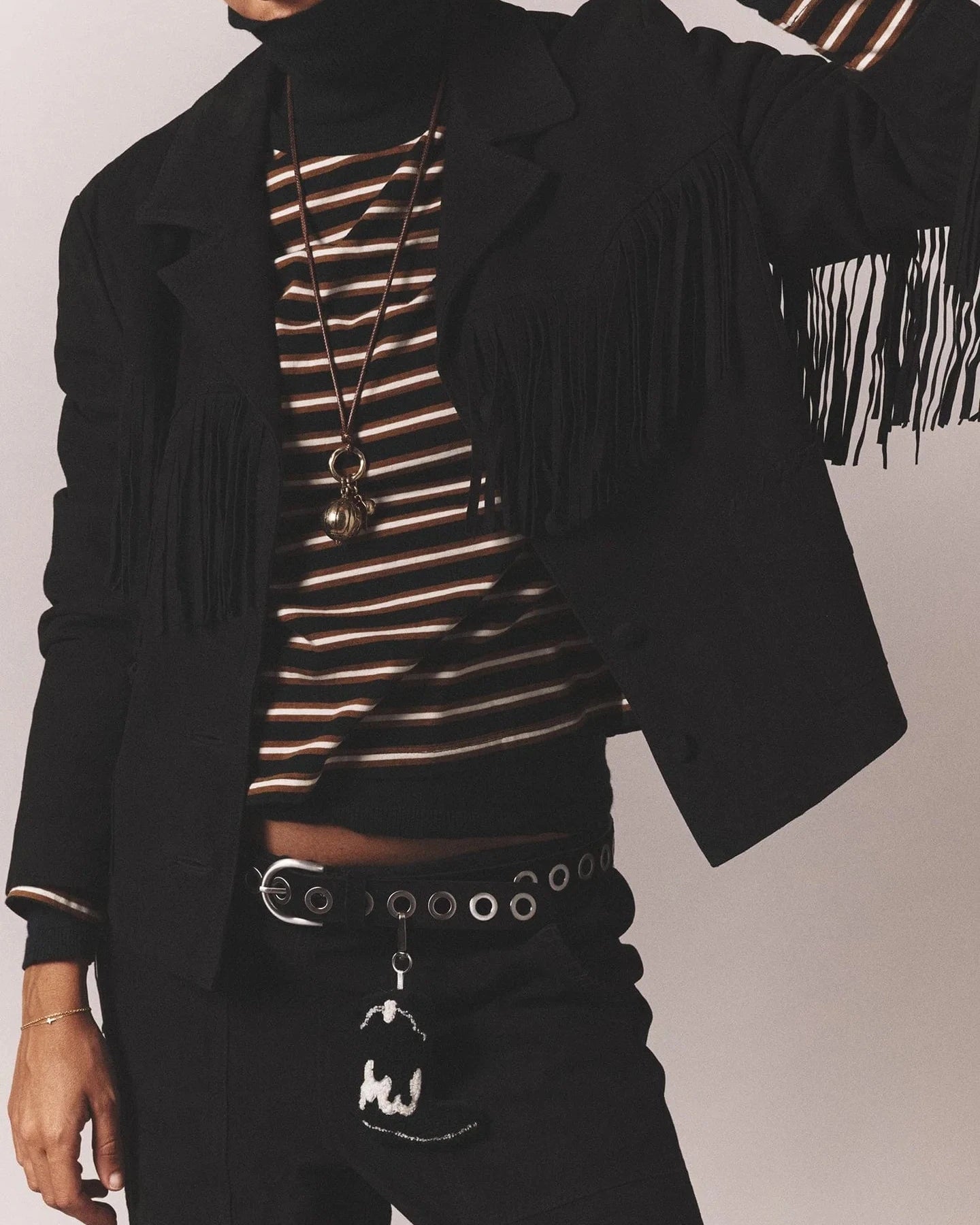 Person wearing a black fringe jacket over a striped top with a plain background