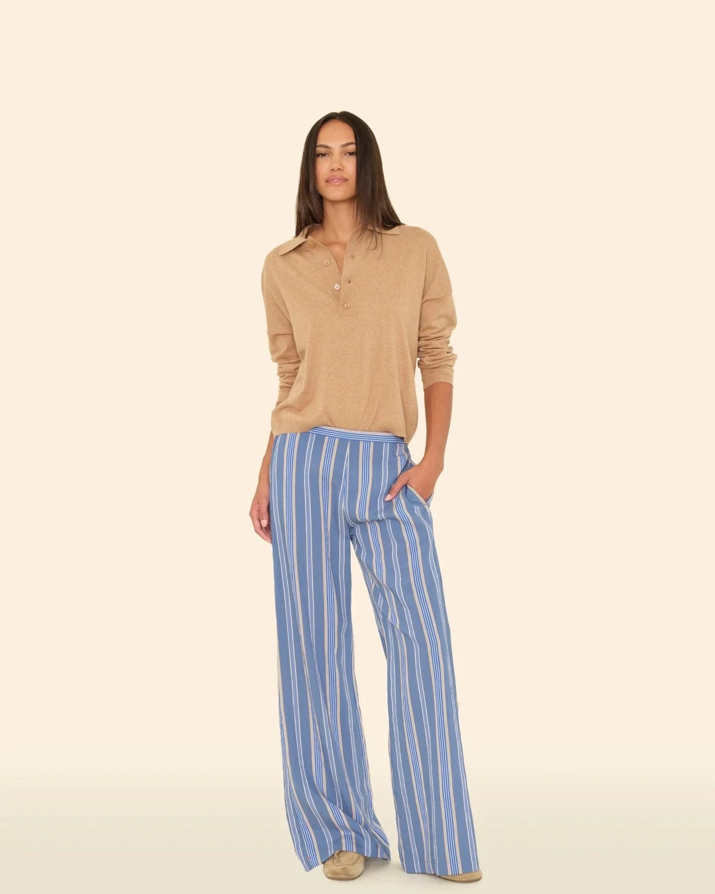Woman wearing a beige top and blue striped pants on a beige background