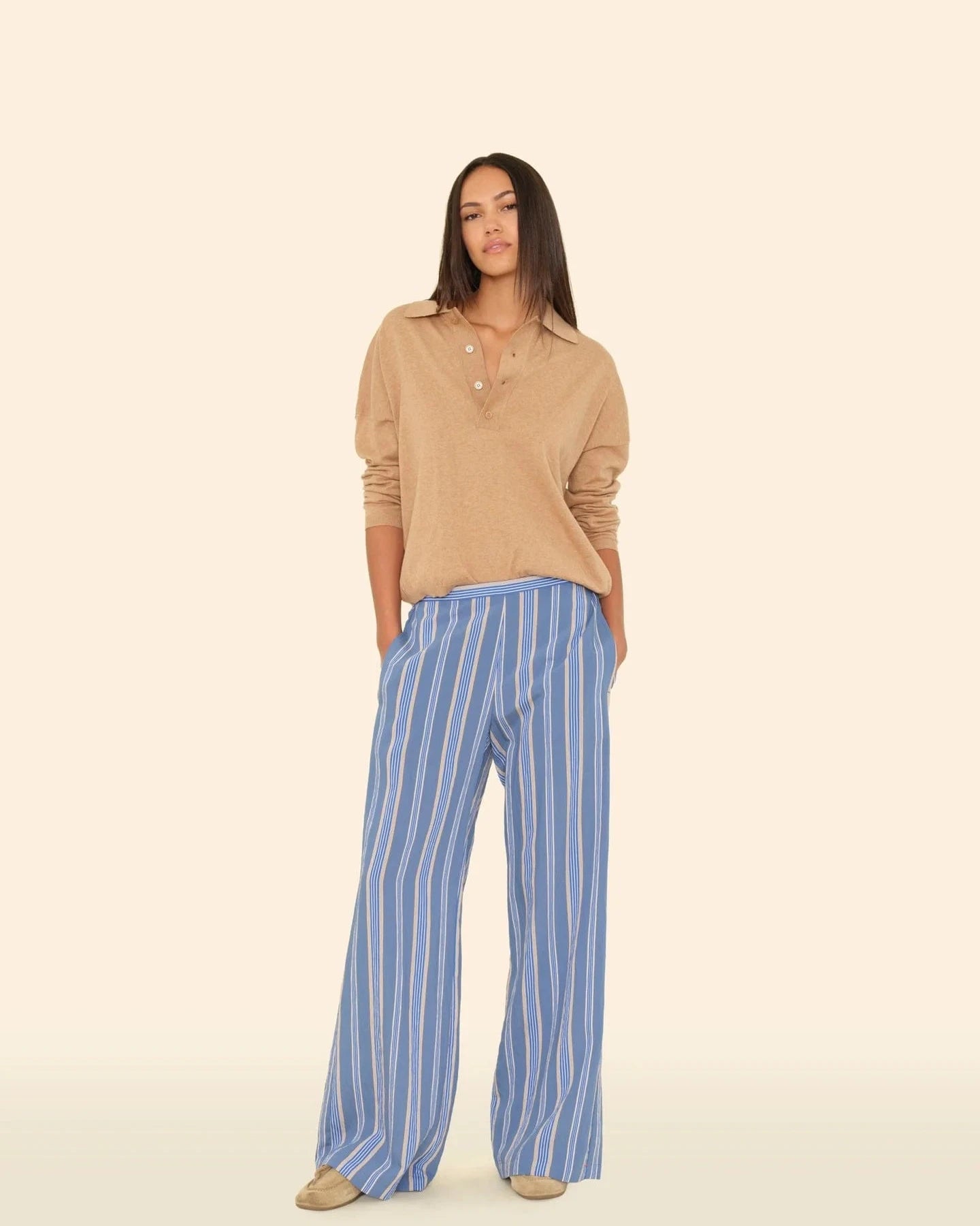 Woman wearing a beige sweater and blue striped pants on a beige background