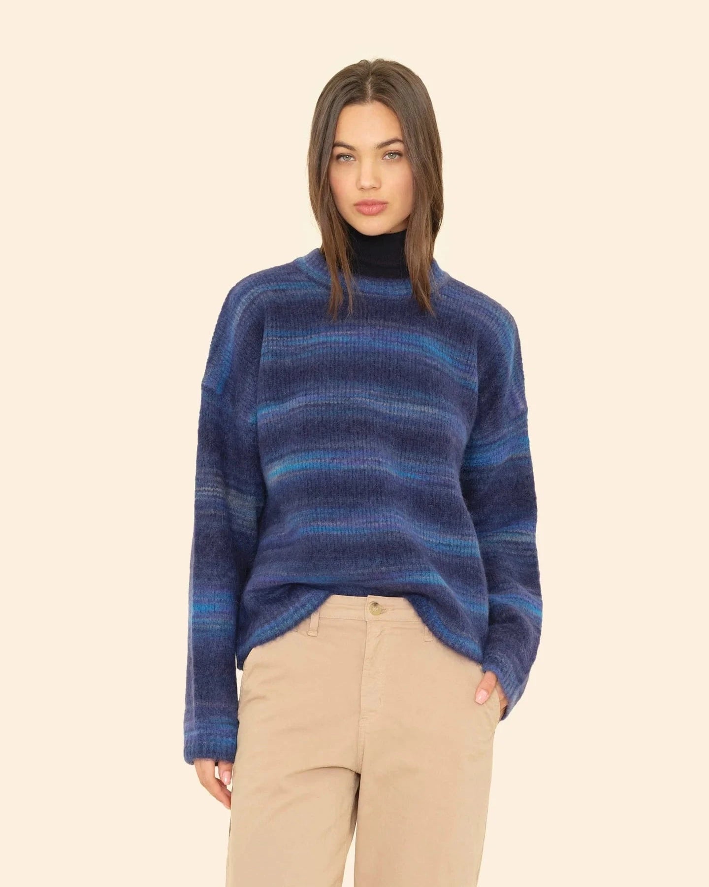 Woman wearing a blue striped sweater and beige pants on a beige background
