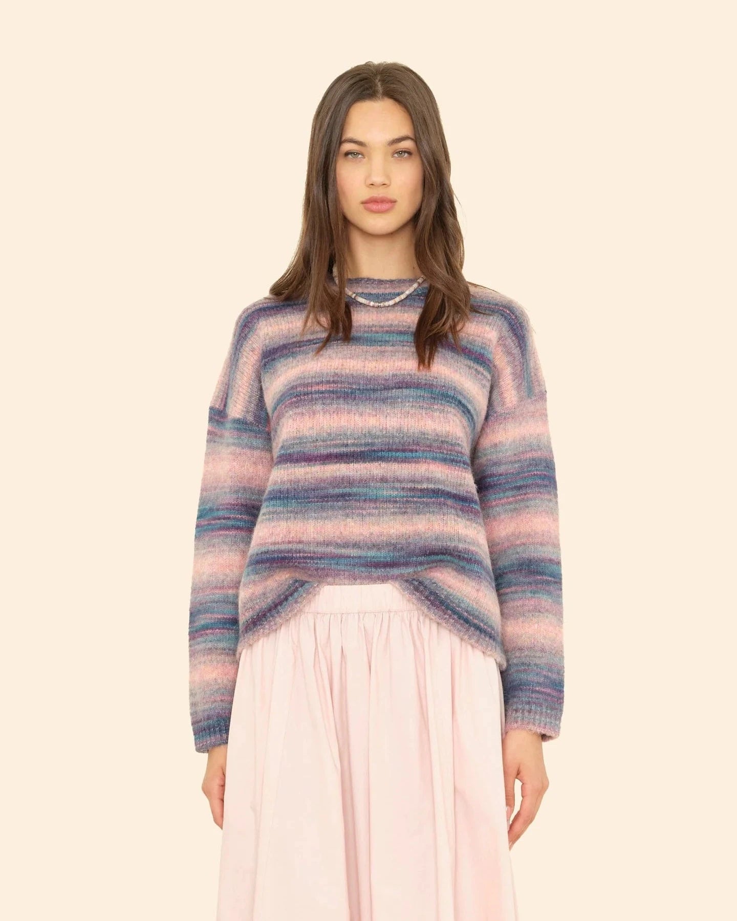 Woman wearing a striped sweater and pink pants on a beige background