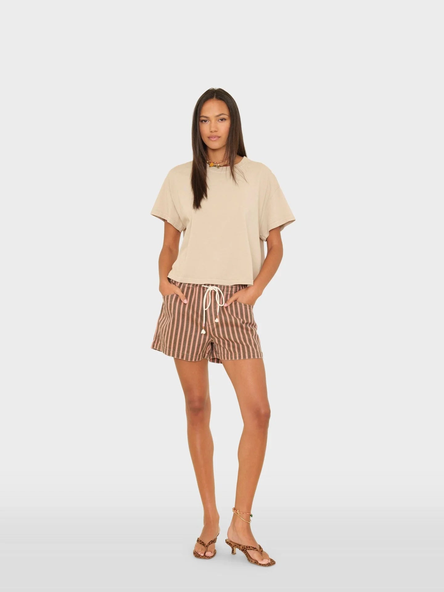 Woman wearing a beige top and striped shorts on a white background