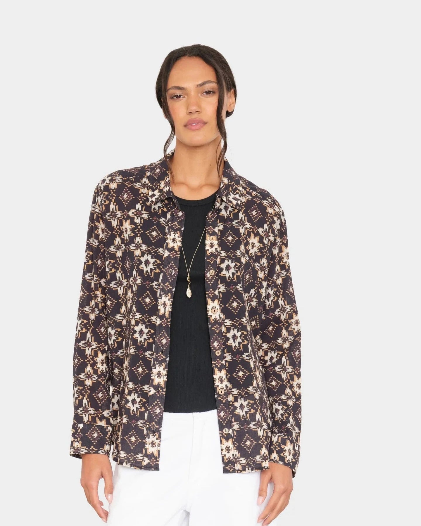 Woman wearing a patterned jacket over a black top and white pants on a light gray background