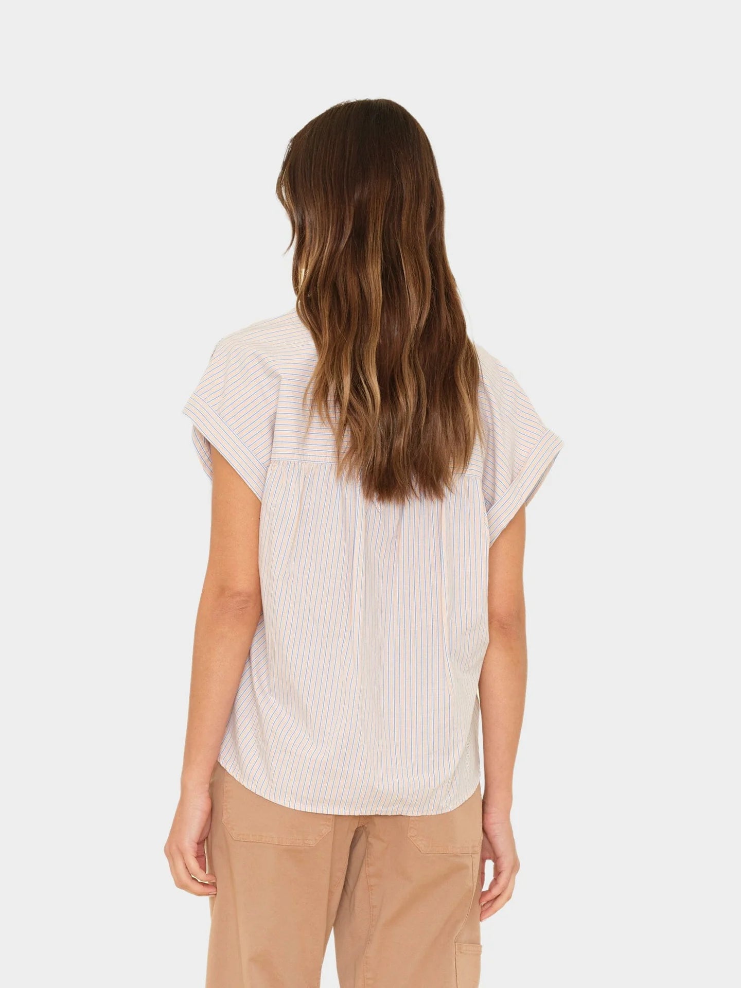 Woman wearing a white ribbed blouse and beige pants on a white background