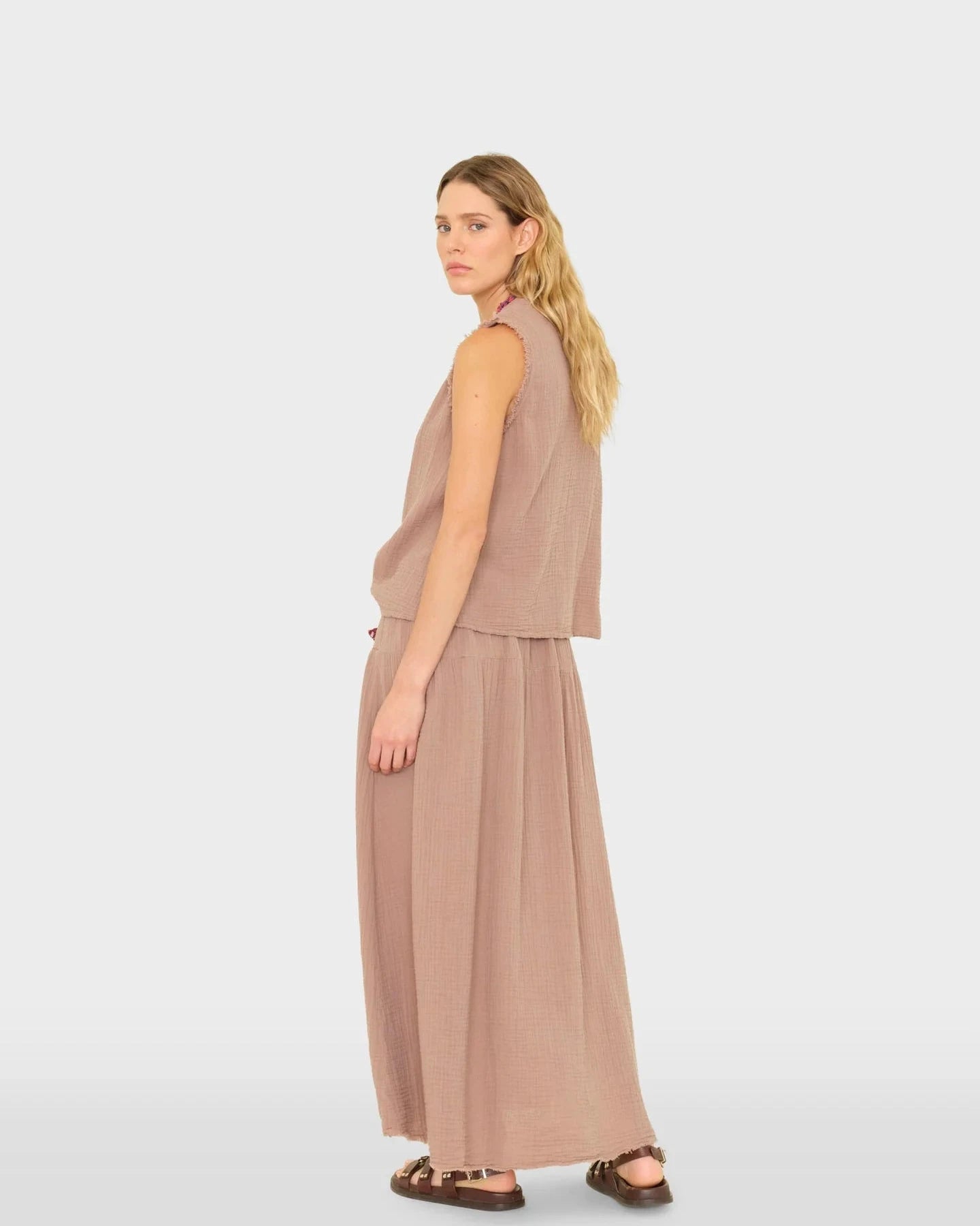 Woman wearing a beige sleeveless top and long skirt on a white background