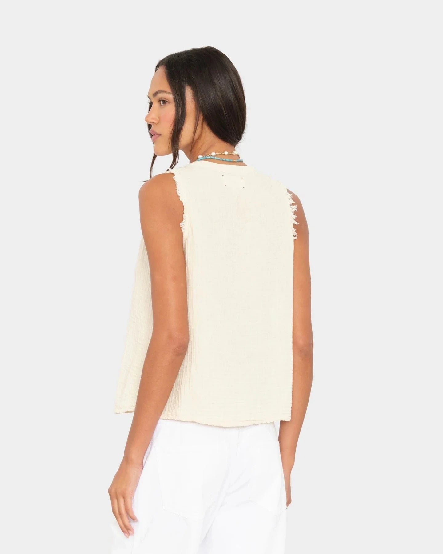Woman wearing a sleeveless cream top with cut-out details on a white background