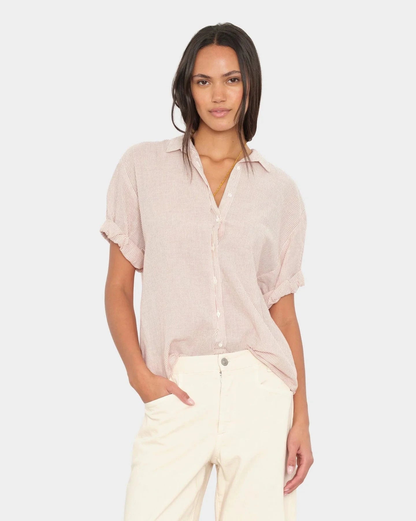 Woman wearing a light pink blouse and white pants on a plain background