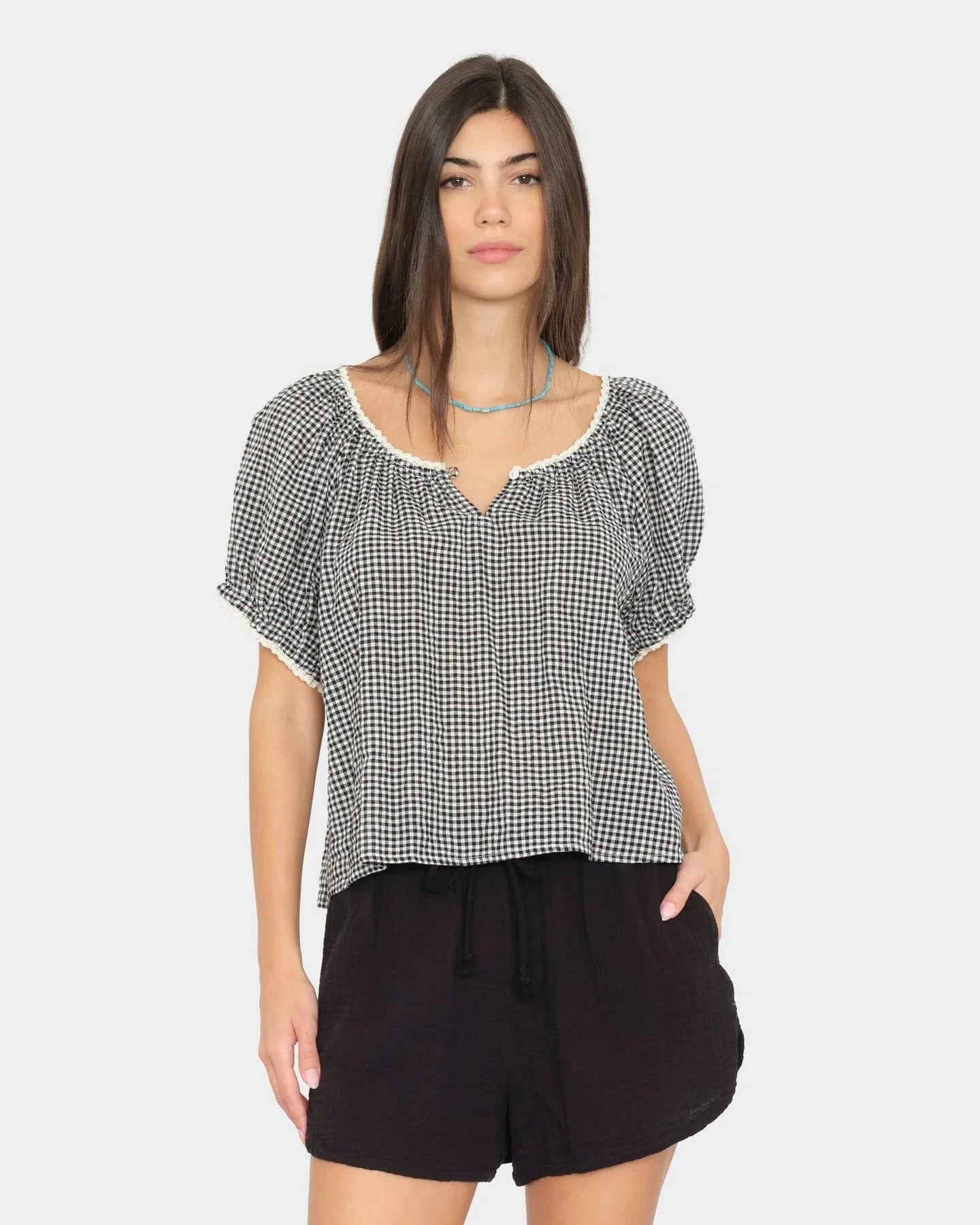 Woman wearing a black and white checkered top with black shorts on a white background
