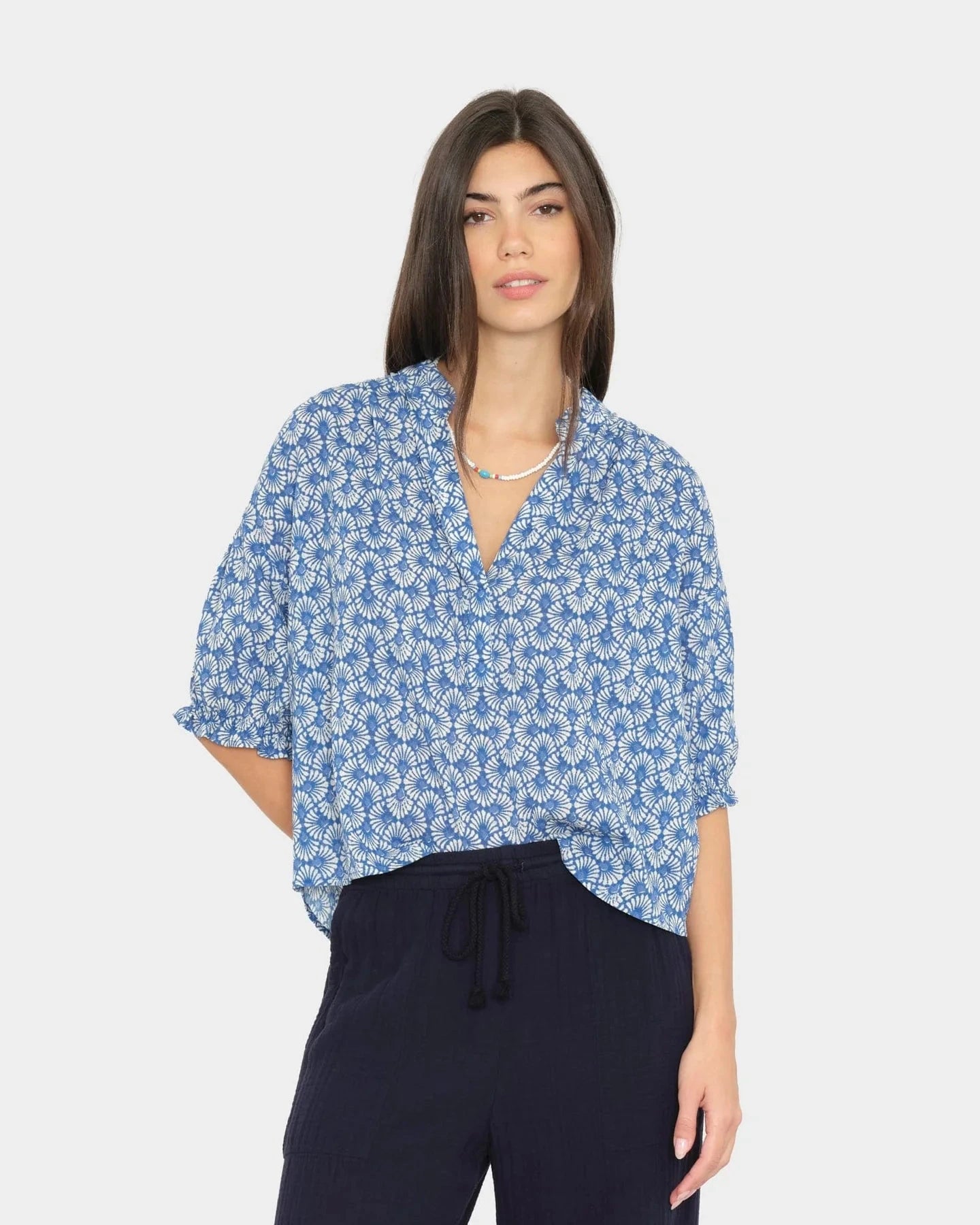 Woman wearing a blue floral blouse and navy pants on a white background