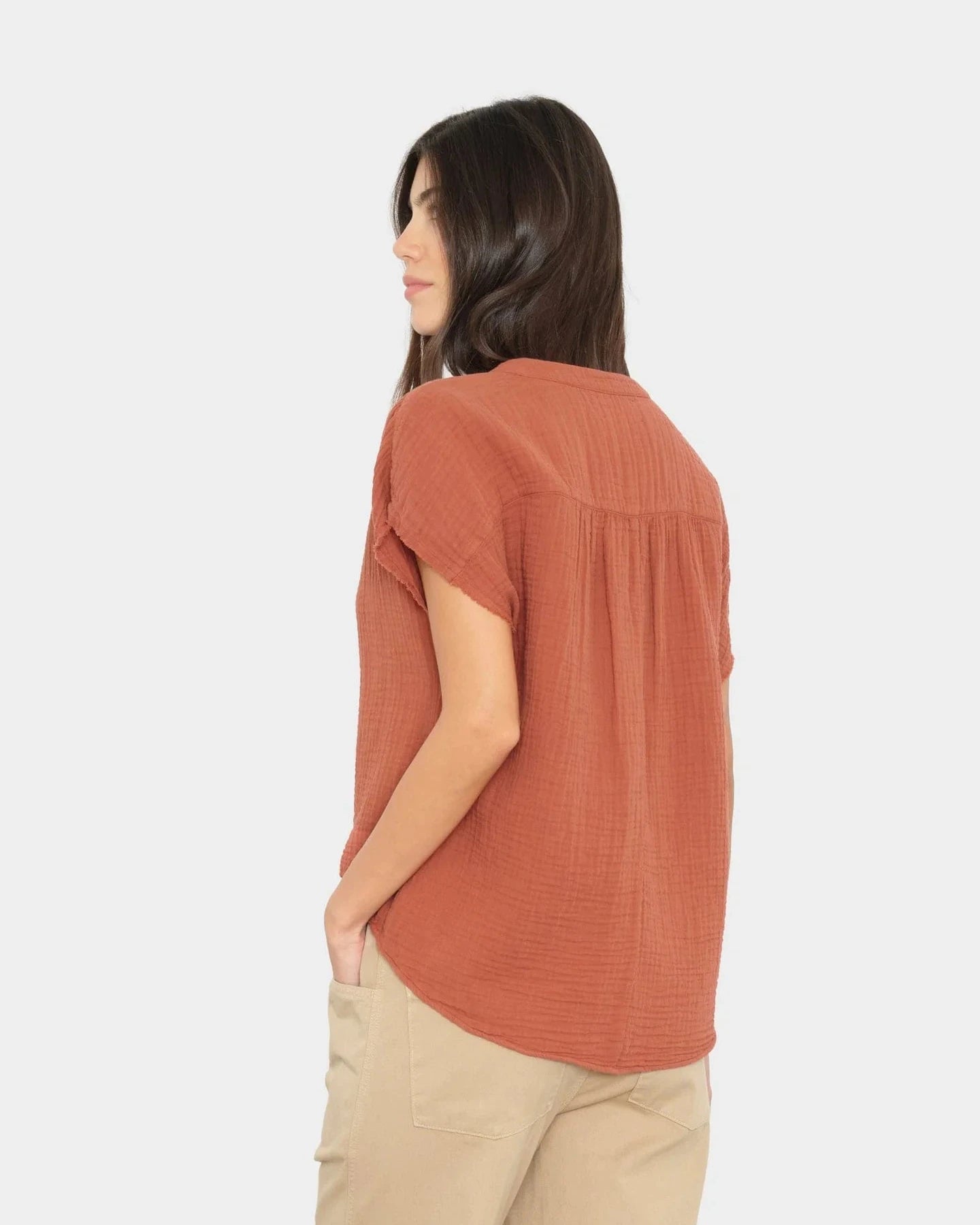 Woman wearing a rust-colored blouse and beige pants on a white background