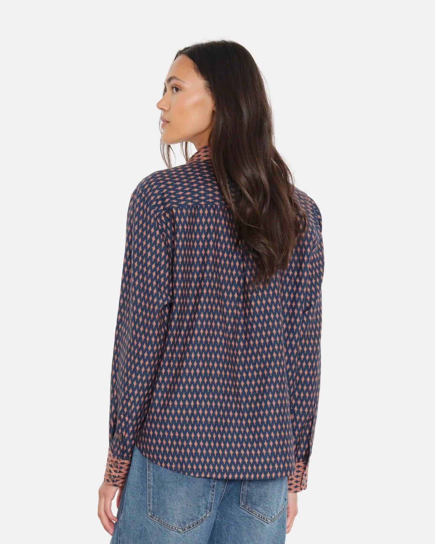 Woman wearing a patterned shirt and jeans on a white background