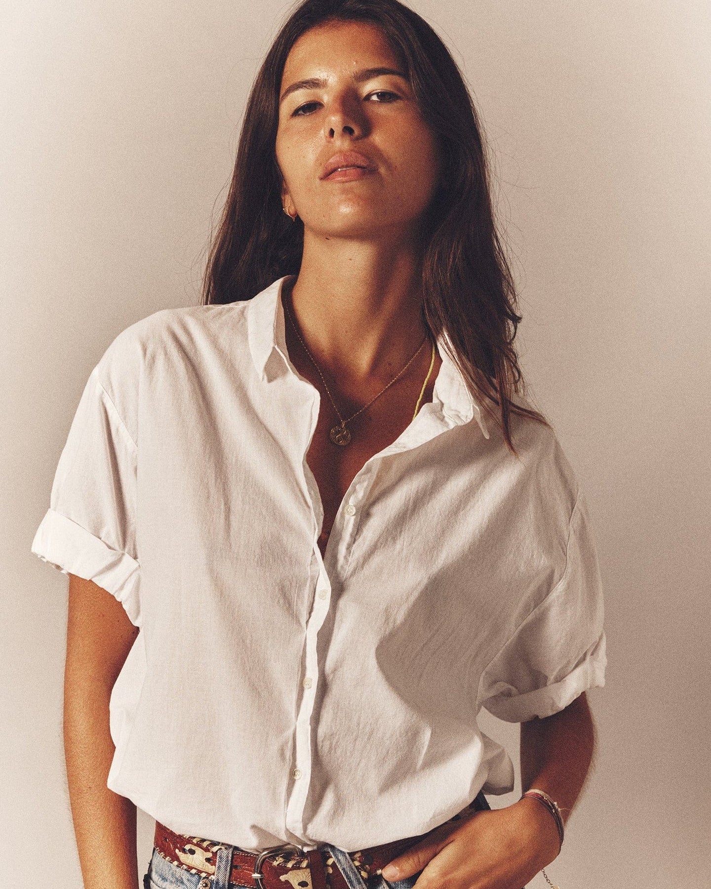 Woman wearing a white shirt with rolled-up sleeves against a plain background